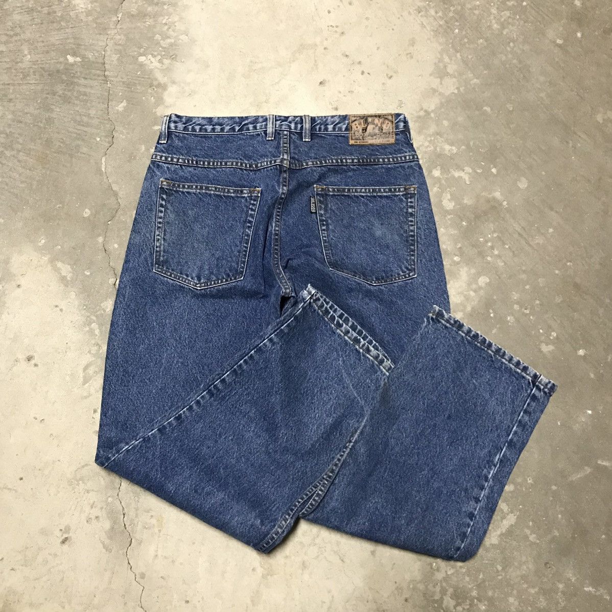 Vintage 1990s baggy blue skate jeans laid flat showing the back pockets, waistband patch and wide legs