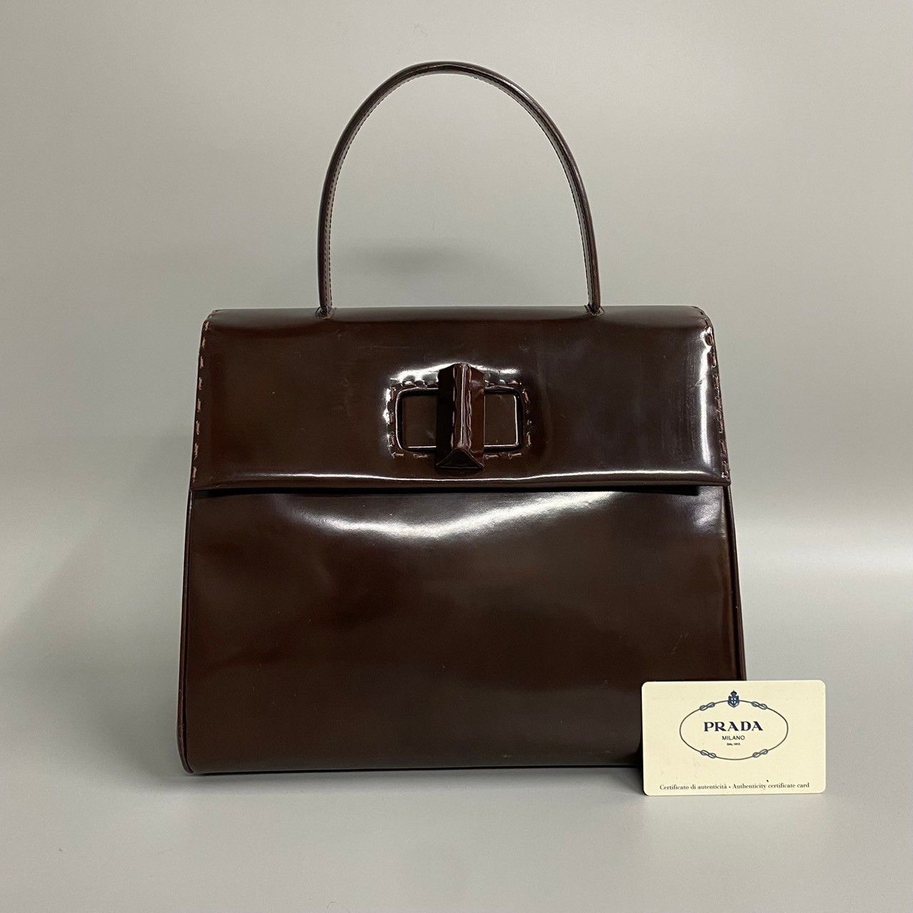 image of Prada Patent Turnlock Top Handle Bag in Brown, Women's
